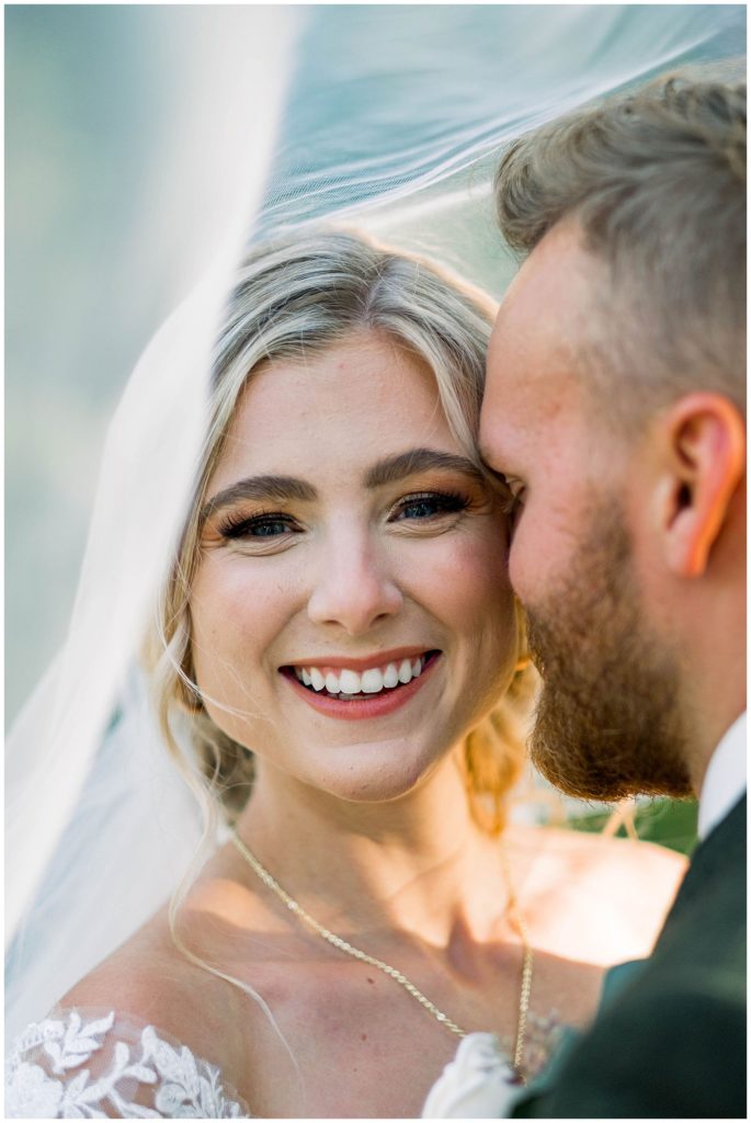 bride smiling while groom whispers in her ear during bridal shot
