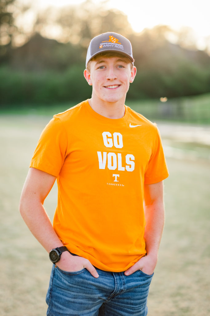 High school senior wearing Vols shirt and army hat during outdoor senior session