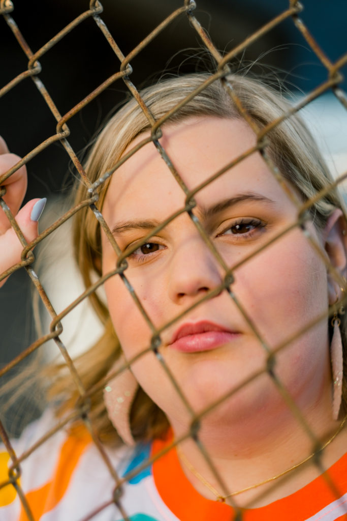 blonde senior looking through chain link fence during session