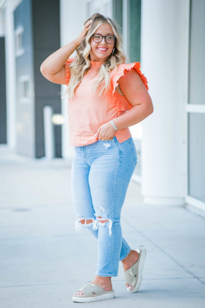 young woman wearing orange top and ripped jeans smiling during outdoor senior session