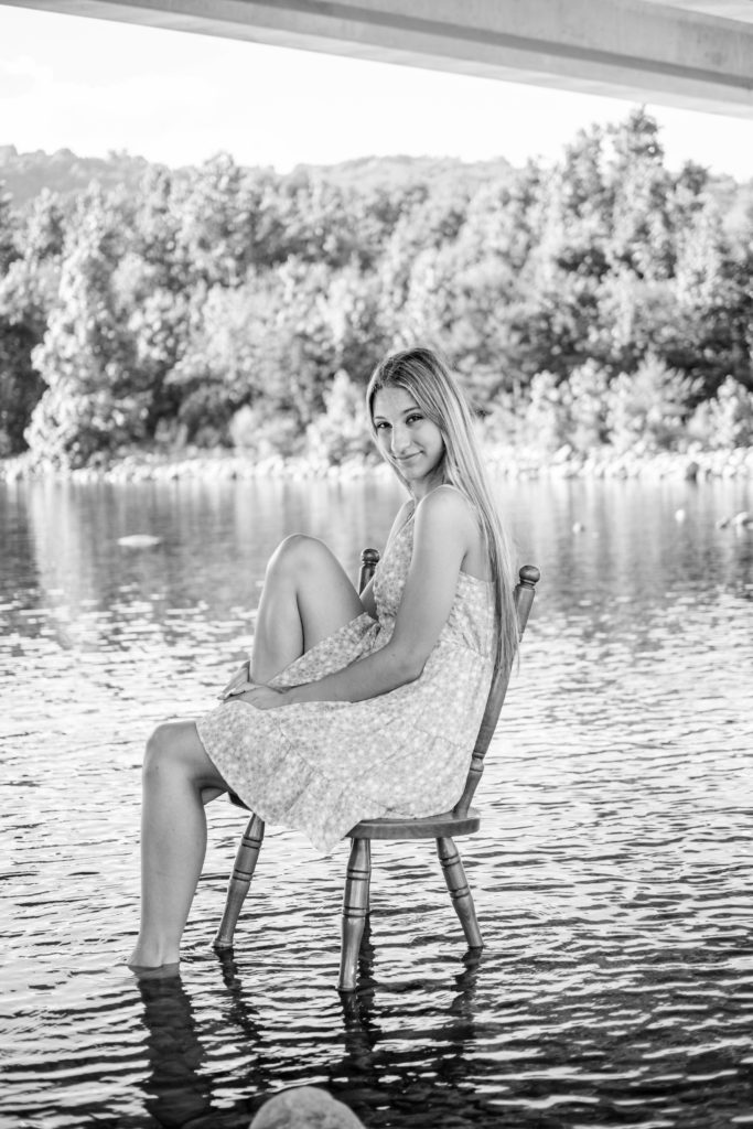 young senior sitting in chair in river during outdoor senior session