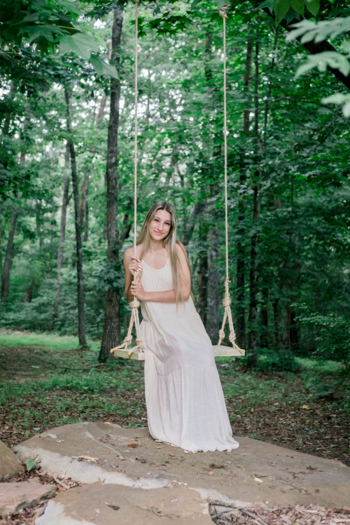 young woman sitting on a swing in the woods in tn for her outdoor senior pictures with the best knoxville senior photographer