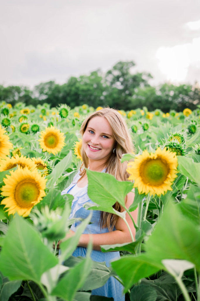 young woman standing in field wearing blue dress during Ooltewah sunflower session
