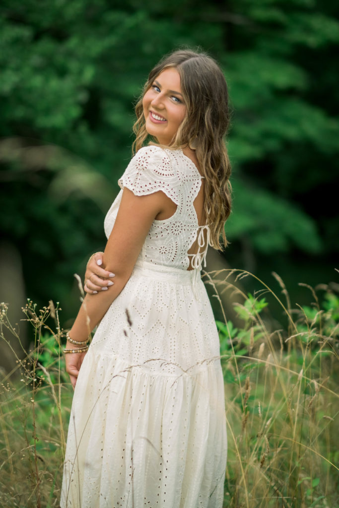 Knoxville senior standing in a field looking over her shoulder and smiling at the camera as she wears a white lace gown