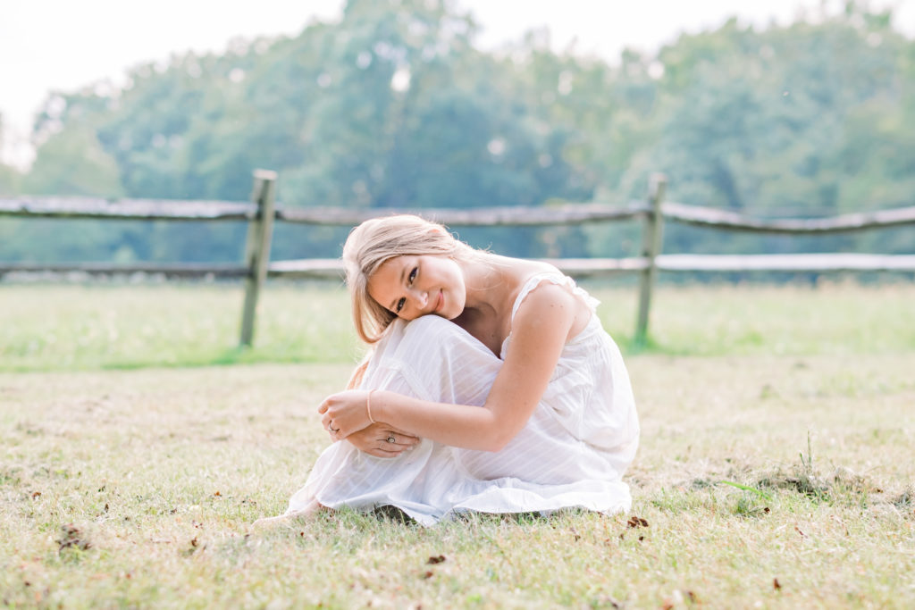 young tennessee senior sitting in grass in field wearing white dress