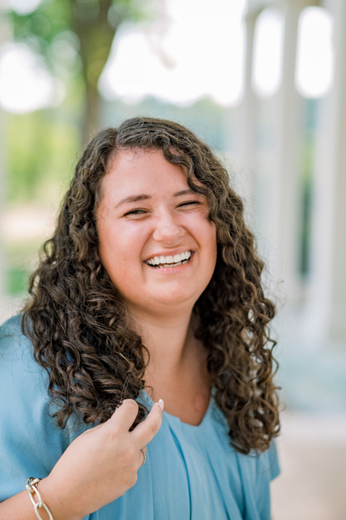 young woman with curly brown hair ina blue blouse laughing during her senior session in Knoxville tn with the best senior pics photographers 