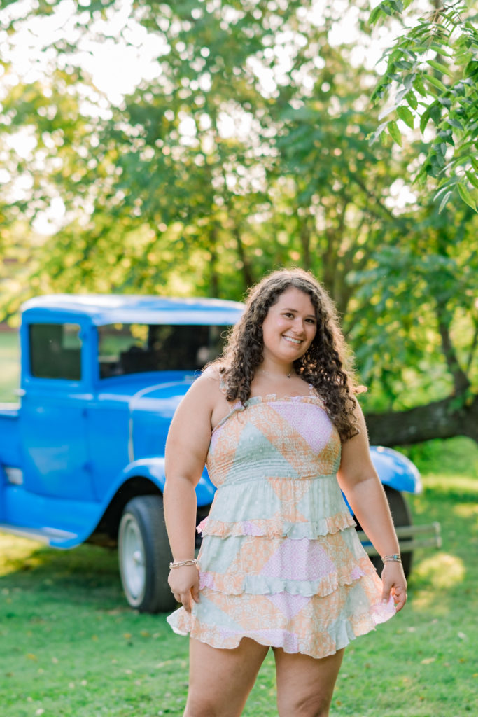 woman standing in front of old blue pickup truck in pink floral dress