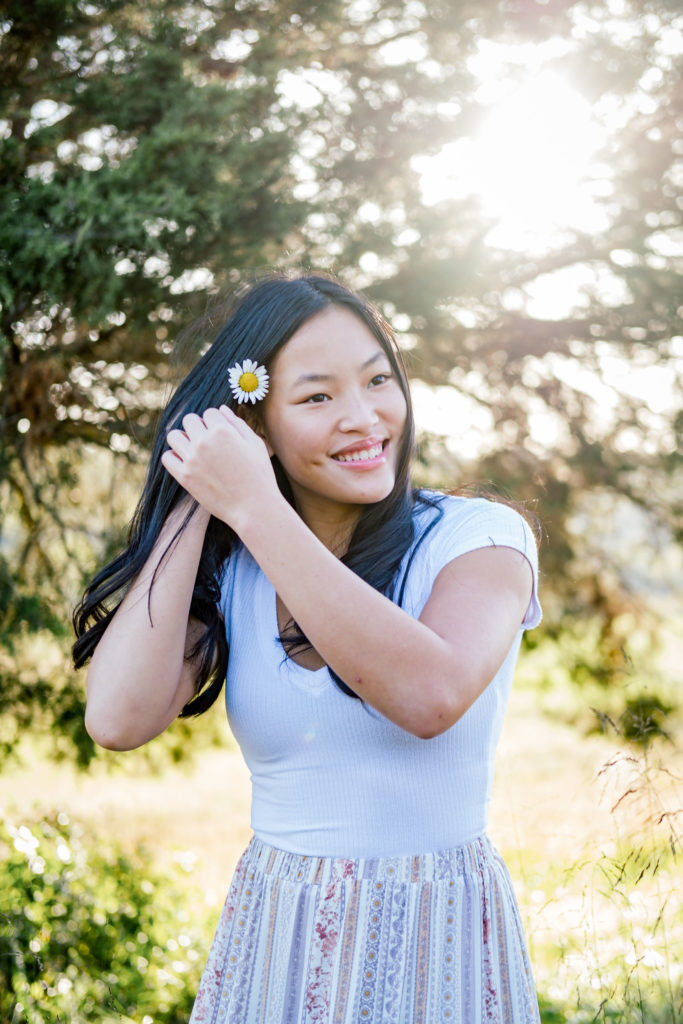 young senior posing wearing white senior pictures dress putting flower in hair