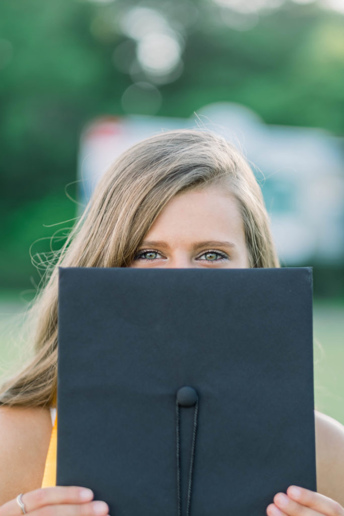 girl holding graduation cap over face