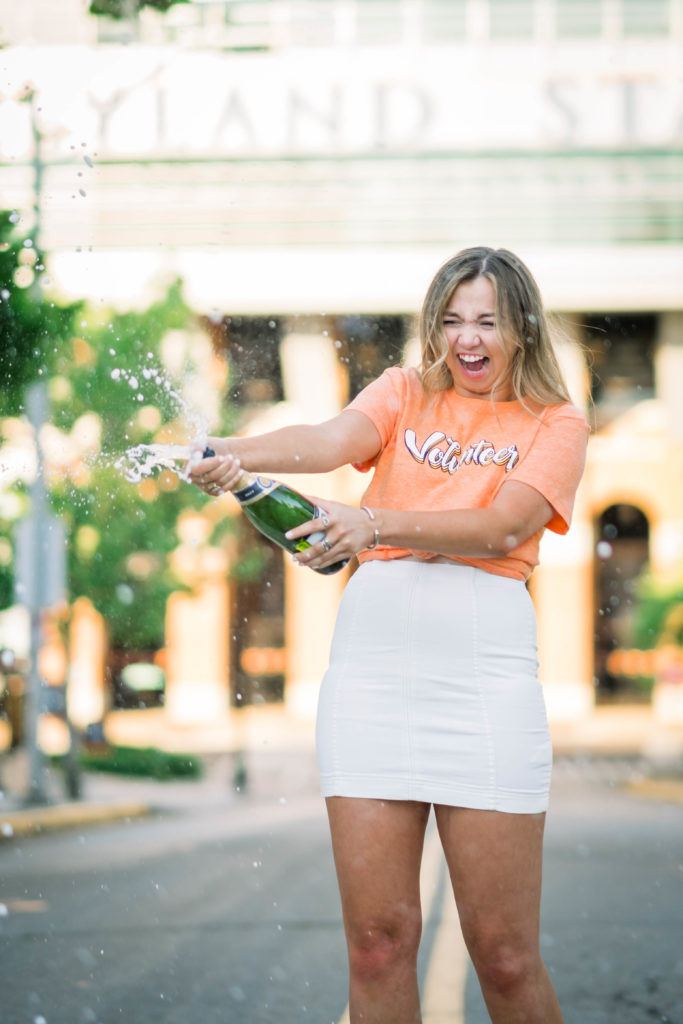 young woman popping champagne celebrating graduation