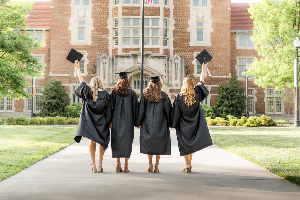 young women standing back to the camera wearing graduation gowns celebrating graduation pictures