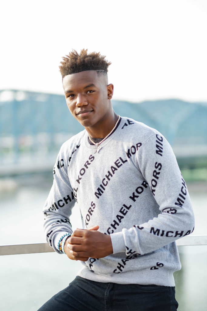 Young man wearing gray sweater smiling during senior portraits