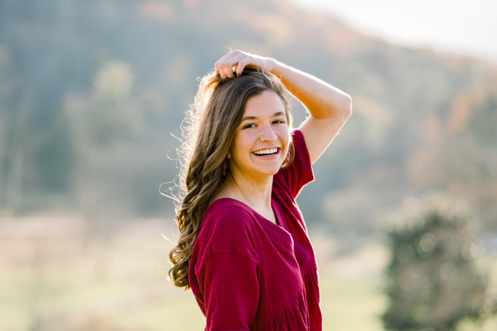 knoxville high school senior portraits at golden hour. Senior is wearing a deep red dress with long brown curled hair.