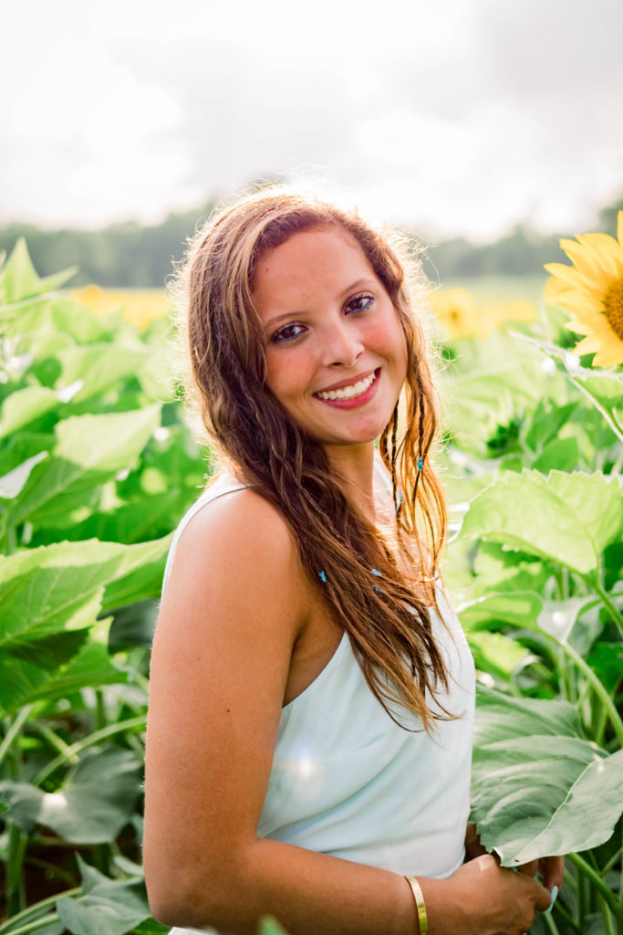 young high school senior smiling and laughing in sunflower field during summer senior session