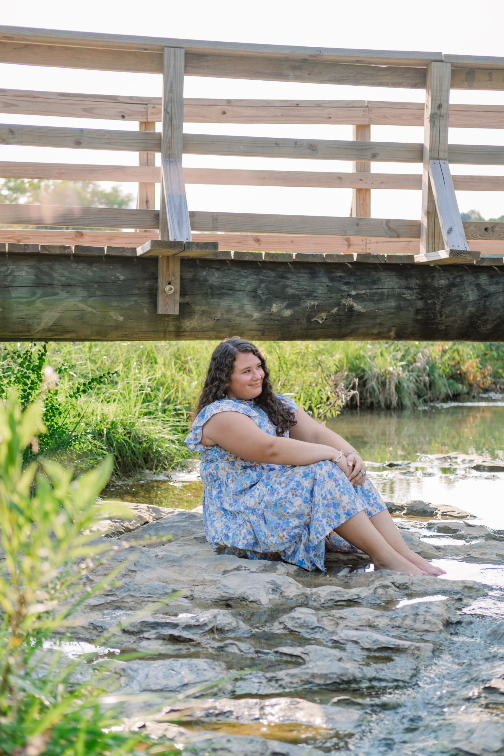 woman sitting on rock near bridge and creek in blue dress