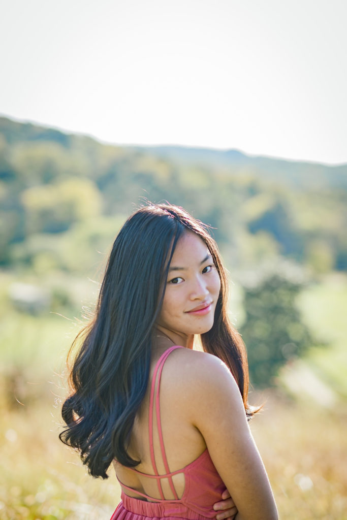 young woman looking over her shoulders wearing pink senior pictures dresses