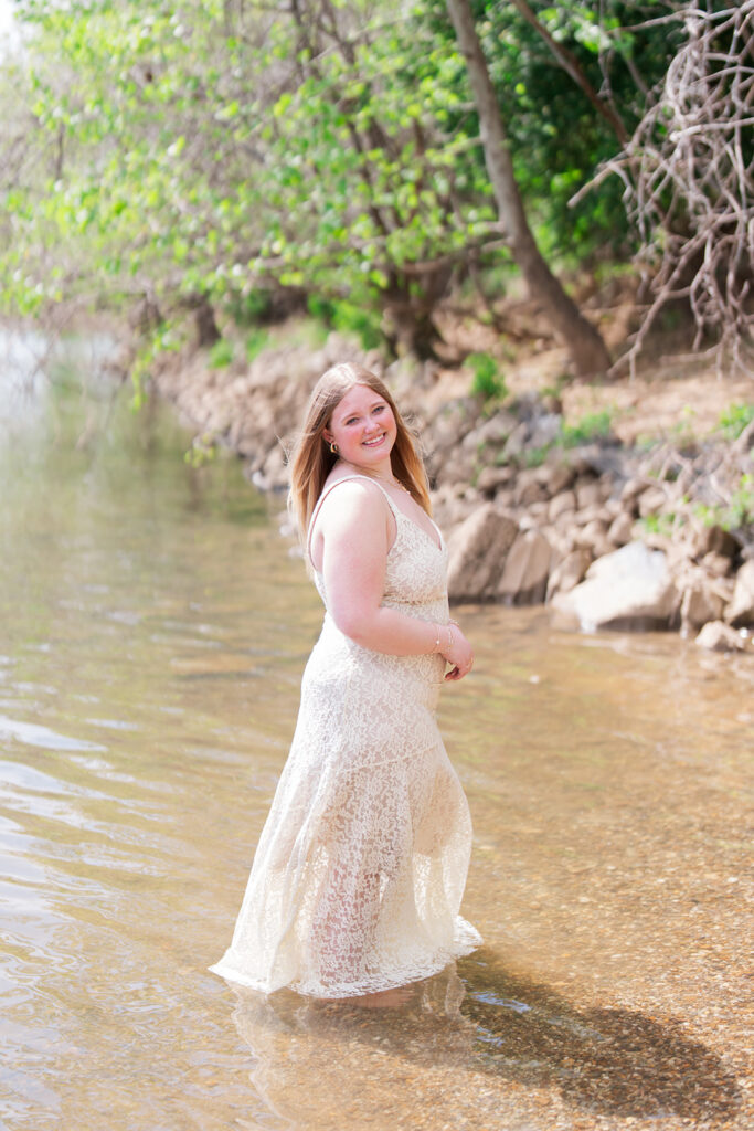 Lauren sitting in the Tennessee River wearing a lace dress | Downtown Chattanooga senior pictures in the river | Bess Pics Photography